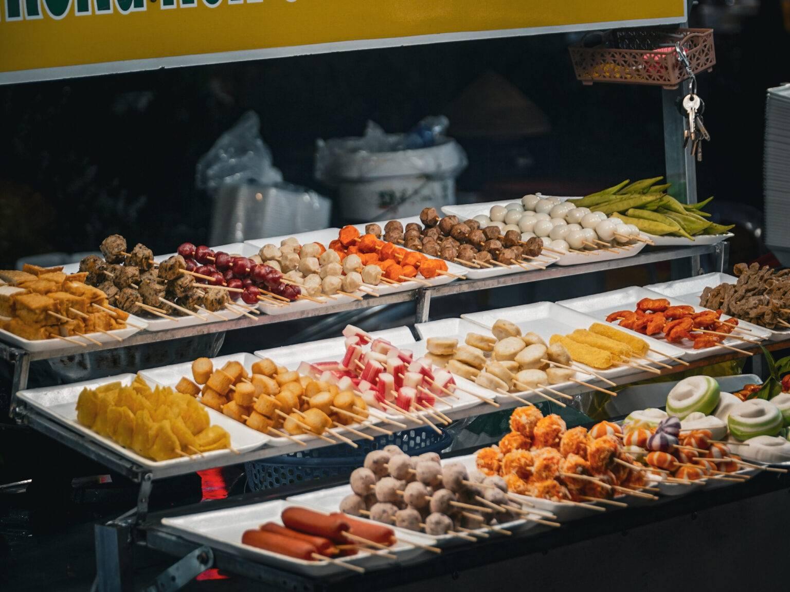 Display of a food stand with many bowls filled with various skewers.