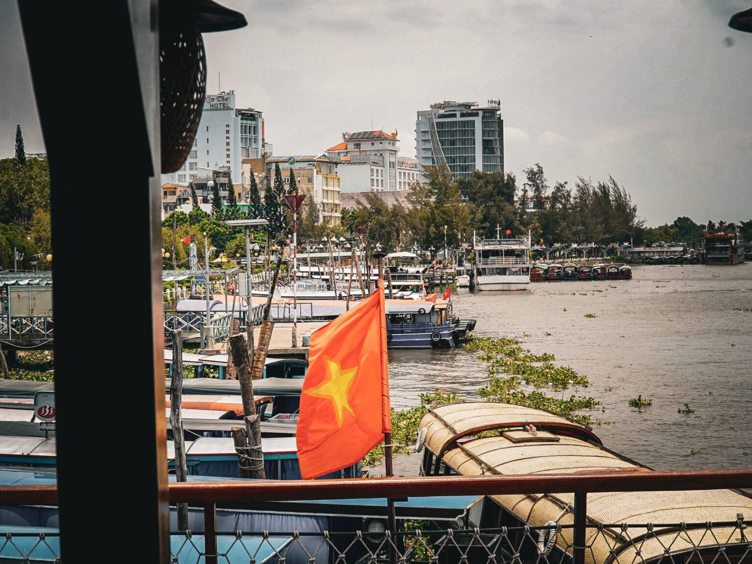 The port of Can Tho with several boats docked. A Vietnamese flag is flying on one boat.
