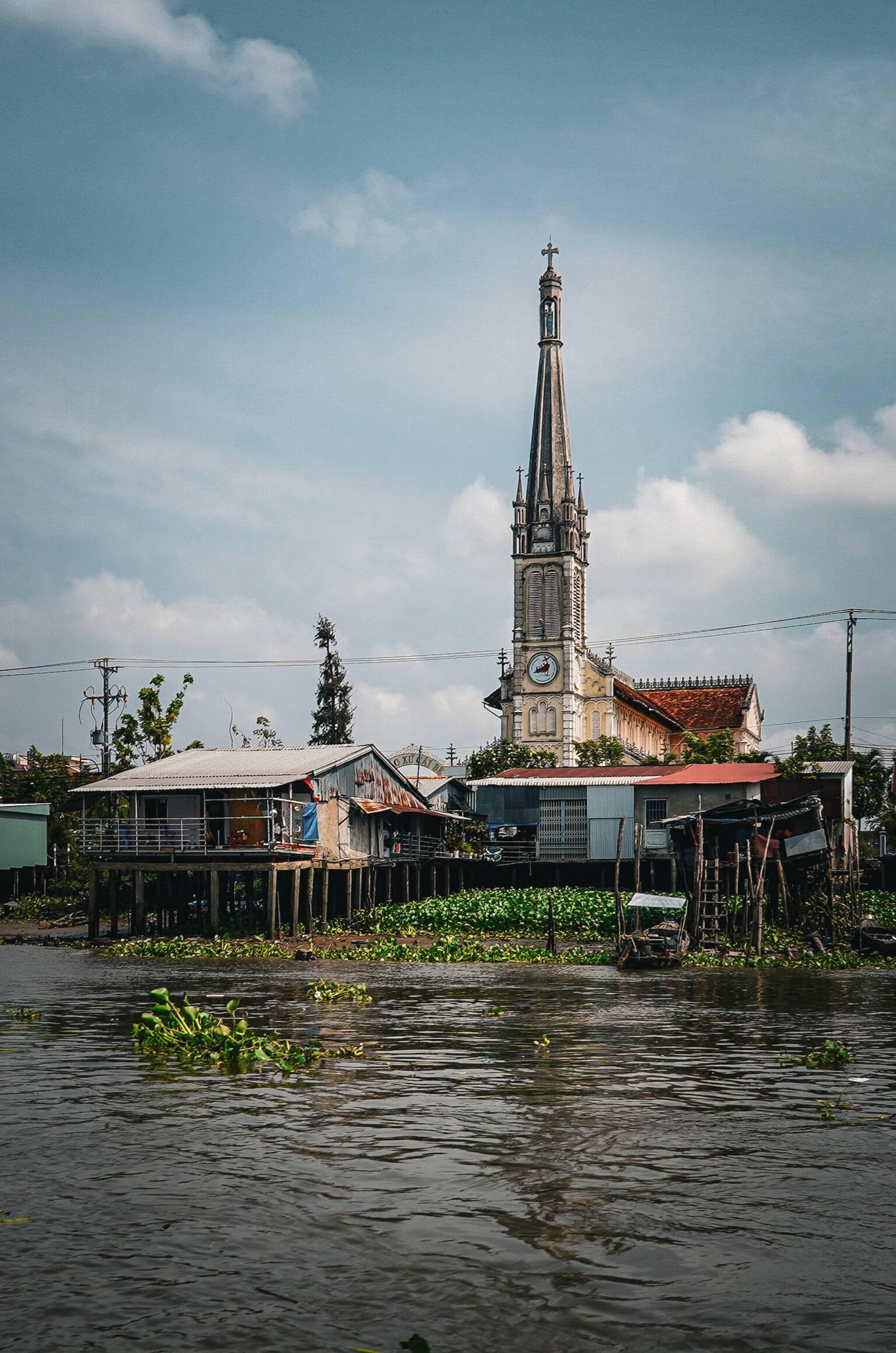 The church of Cai Be with a tall spire and the river in the foreground.