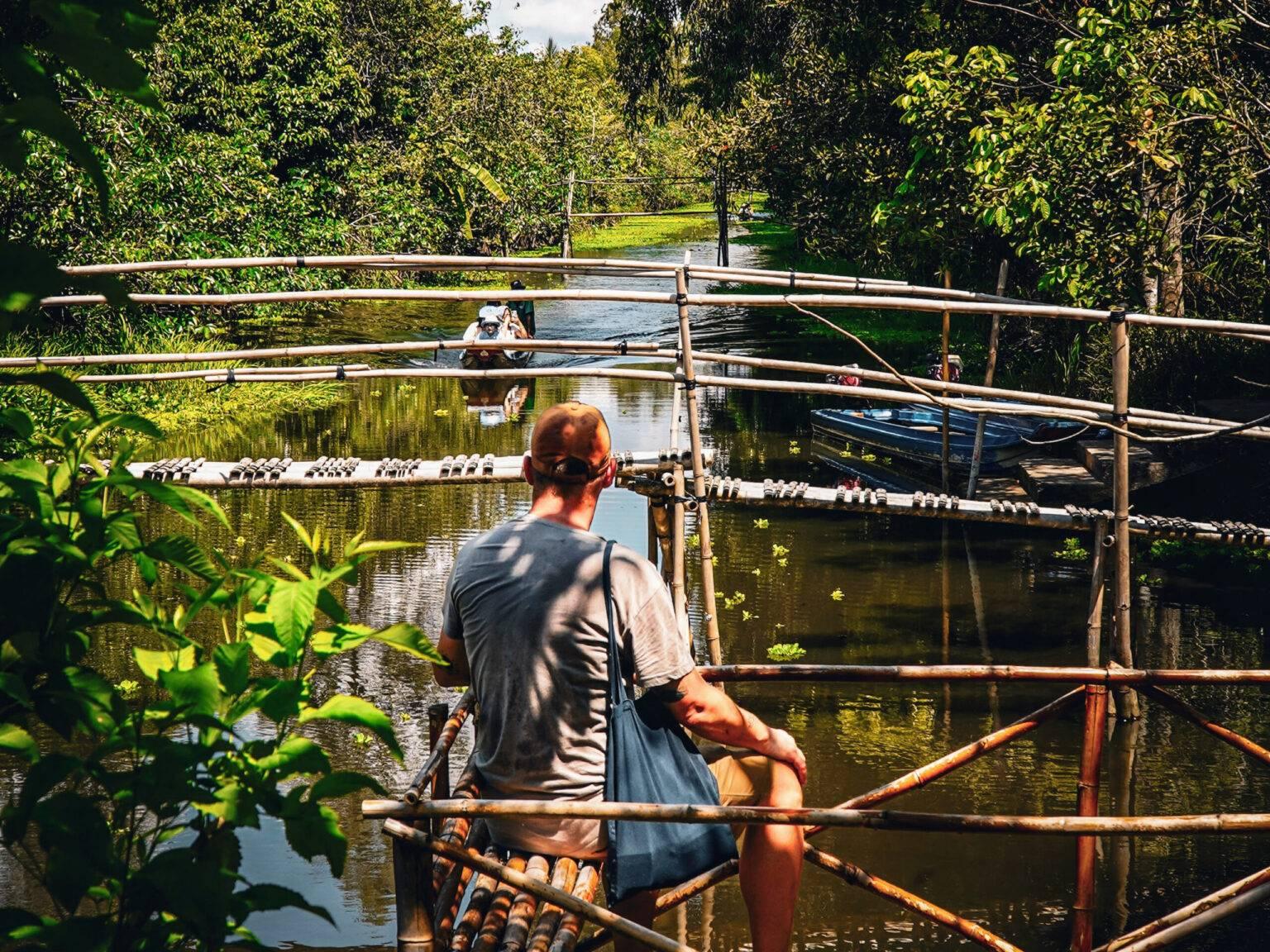 Daniel sits on a bamboo structure by the shore of a small river in Lung Ngoc Hoang Reserve.