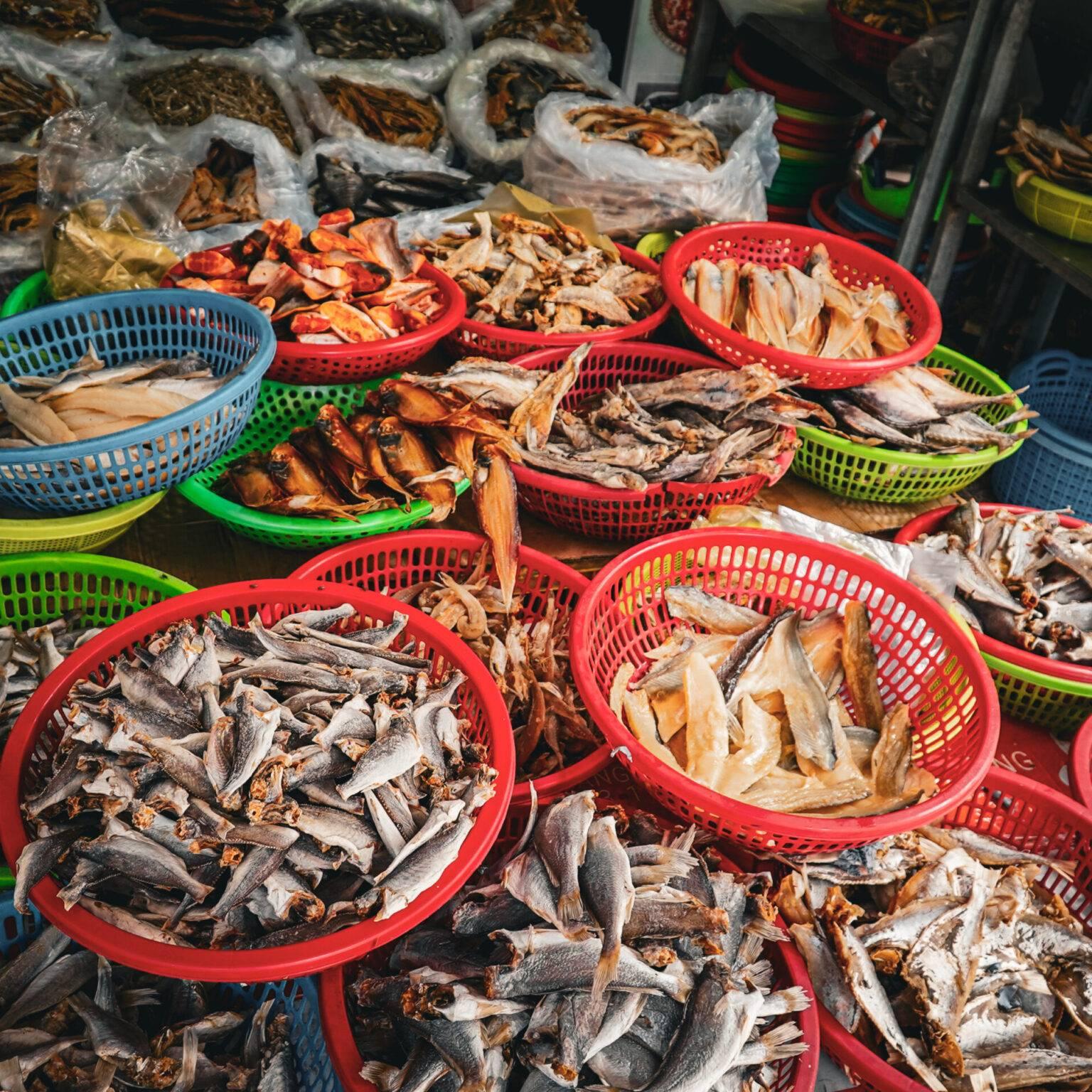 Street stall at the Cai Be market with bowls full of dried fish.
