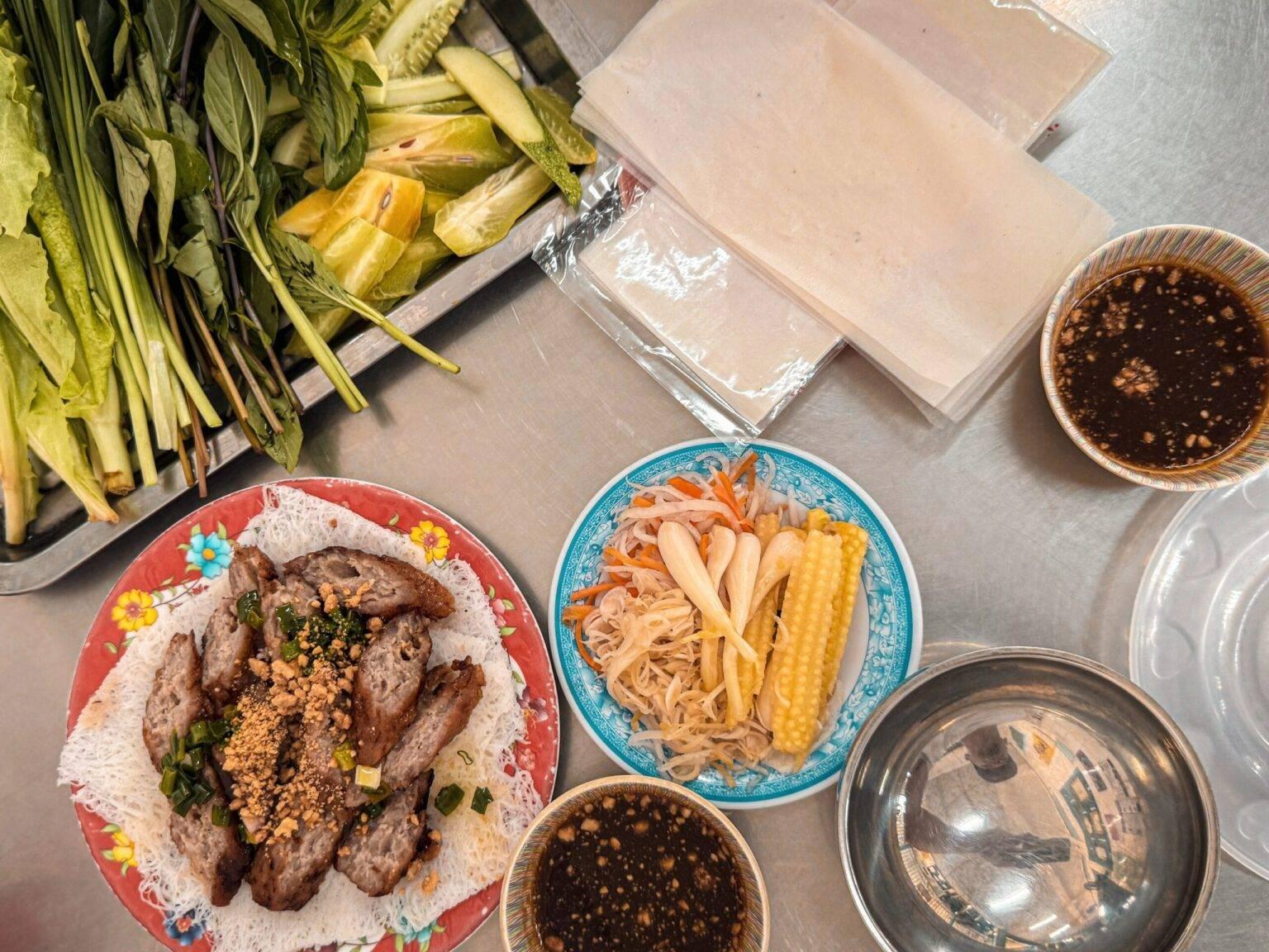 A table with several bowls and plates filled with meat, raw veggies, and sauces.