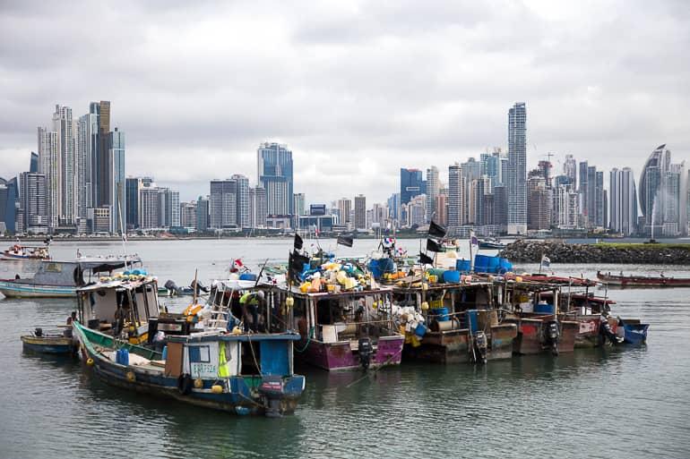 Barcos de pesca completamente cargados navegan en el puerto frente al horizonte de la ciudad de Panamá.