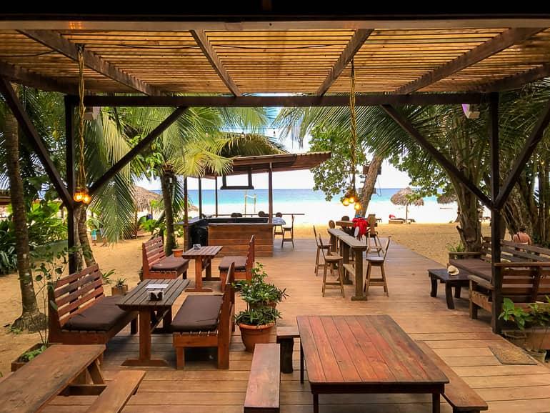 En la acomodación Palmar en la isla Bastimentos hay una terraza de madera con sillas entre palmeras y vista a la playa.