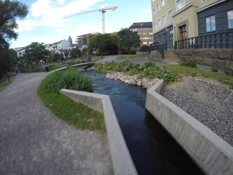 Un pequeño arroyo rodeado por muros de hormigón fluye junto a una acera en Norrköping, Östergötland.