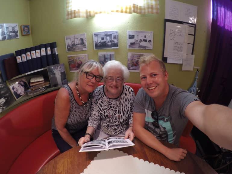 Dos damas se sientan con el bloguero en un sofá de cuero rojo redondo, la señora mayor en el medio sostiene un libro de fotos de Zarah Leander en las manos.