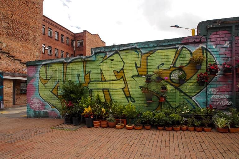 In front of a graffiti-covered wall in downtown Bogotá, many different containers with plants stand.