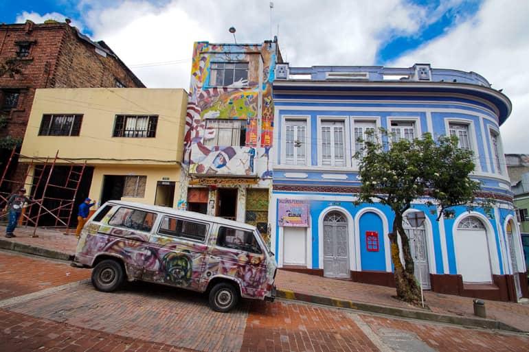 A colorfully spray-painted VW bus stands in the streets of Colombia's capital Bogotá. In the background, graffiti decorates the building facade.