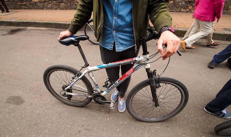 In the streets of Colombia's Bogotá, a man holds his bicycle, the camera's focus is on his bike.