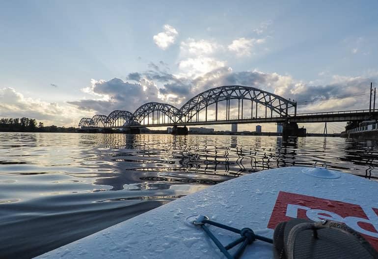 Detrás de las nubes, el sol se pone sobre el río Daugava y el puente ferroviario en el extremo sur del casco antiguo de Riga.
