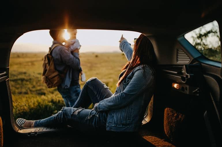 Parental Leave: A woman sitting in the trunk while a man stands with a child in arms in front of her.