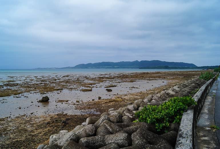 On the Yaeyama island of Ishigaki in Japan, the rain obscures the view of the rocky beach and the wooded hills on the horizon.