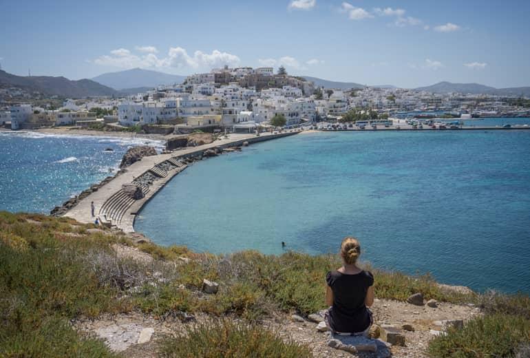 Una mujer sentada en el suelo de un mirador mirando hacia el mar y la ciudad.