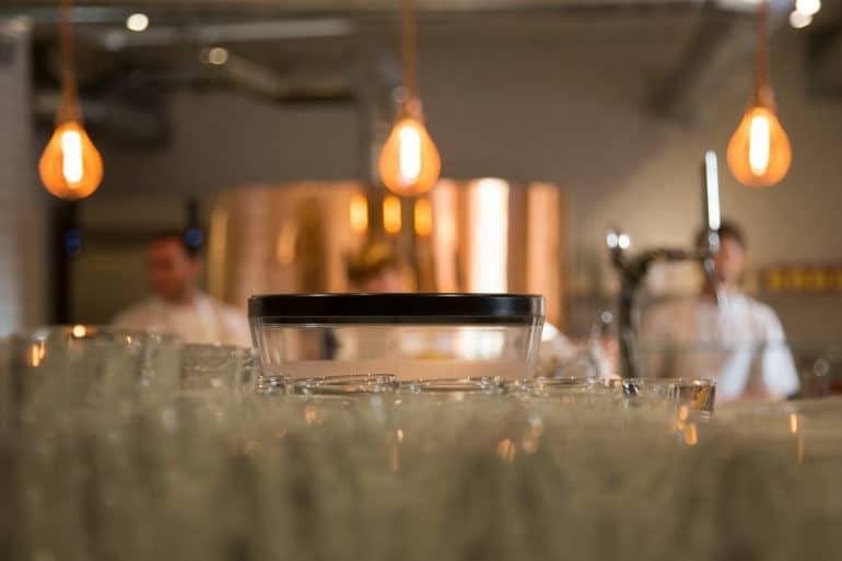 A blurred view through glasses and three hanging light bulbs of the chefs at Pizzeria Pi Shop in Bristol, England.