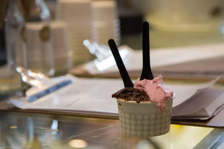 On the counter of Swoon Gelato in Bristol, England, a bowl of ice cream with two black spoons of chocolate and strawberry ice cream is served.