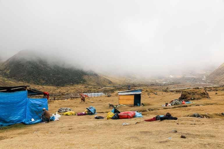 A campsite on the way to Machu Picchu with small huts and tents in the fog, mountains visible in the background.