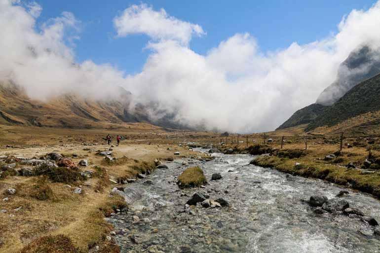 At a river, near a mountain valley, two hikers are on their Salkantay Trek in Peru.
