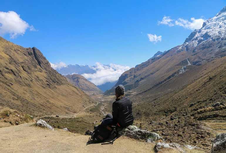 The blogger Manuela sits with her back to the camera enjoying the mountain view while hiking to Machu Picchu in Peru.