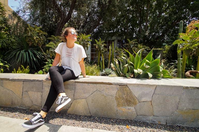En un pequeño saliente de la pared en Melrose Place en Los Ángeles, una mujer disfruta de la vista al sol, con cactus floreciendo detrás de ella.