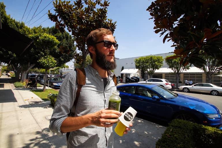 Un hombre camina por las calles de Los Ángeles y sostiene en ambas manos jugos saludables y ricos en vitaminas.