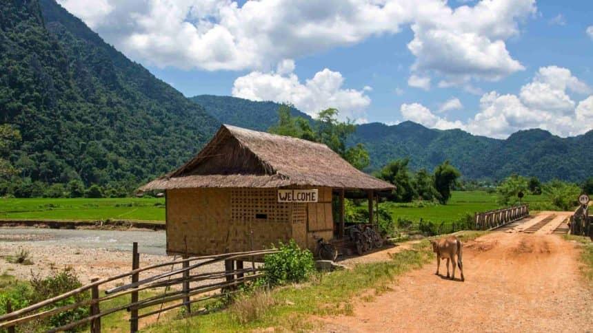 The sandy roads around Vang Vieng in Laos offer a green mountain panorama, small straw huts, and occasionally cows crossing the path.