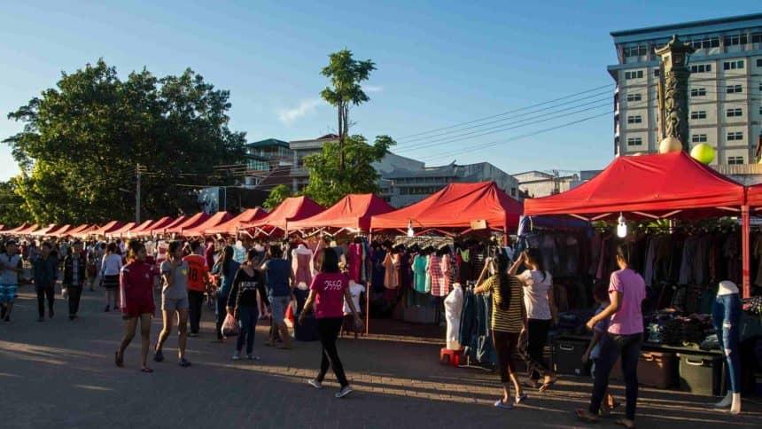The night market at Anouvong Park along the Mekong River in Laos features many small stalls with red umbrellas, selling a variety of souvenirs and clothing.