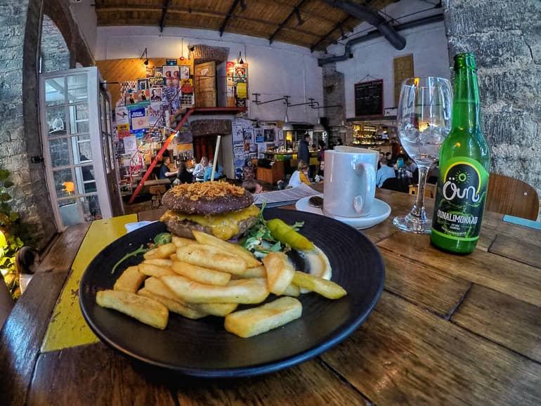 In Tallinn's restaurant F-hoone, burgers with fries are served at a wooden table, with a wall of colorful posters in the background.