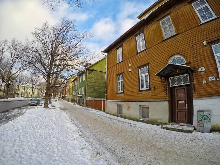 The view of the streets of Tallinn's Kalamaja district shows colorful wooden houses with snow on the sidewalk.