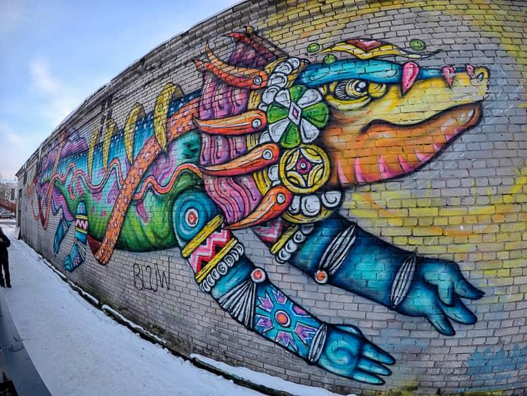 In the Kalamaja district of Tallinn, a colorful dragon is seen as graffiti on a high wall protrusion.