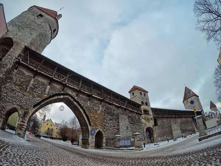 A street leads through the large archway of the old city wall of Estonia's capital Tallinn, with three watchtowers reminiscent of times past.