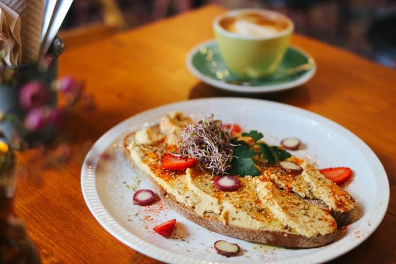 En Mama Carmen's Café en Santa Catalina, Palma, se sirve pan de masa madre casero con hummus, adornado con brotes y fresas para el desayuno, además de cappuccino.