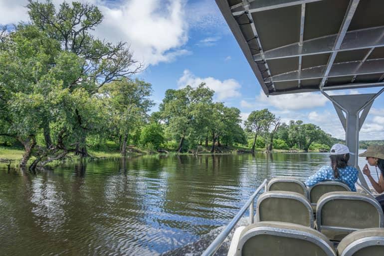 A boat cruises along the Chobe River with two tourists on board.