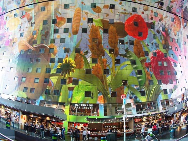 El Mercado de Róterdam por dentro alberga una enorme fachada de vidrio con flores pintadas y muchas diferentes tiendas, donde se agolpan las personas.