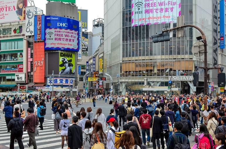 Amidst the intersection in the heart of Shibuya, Japan, many people gather; the building facades are cluttered with all sorts of advertisements and signs.
