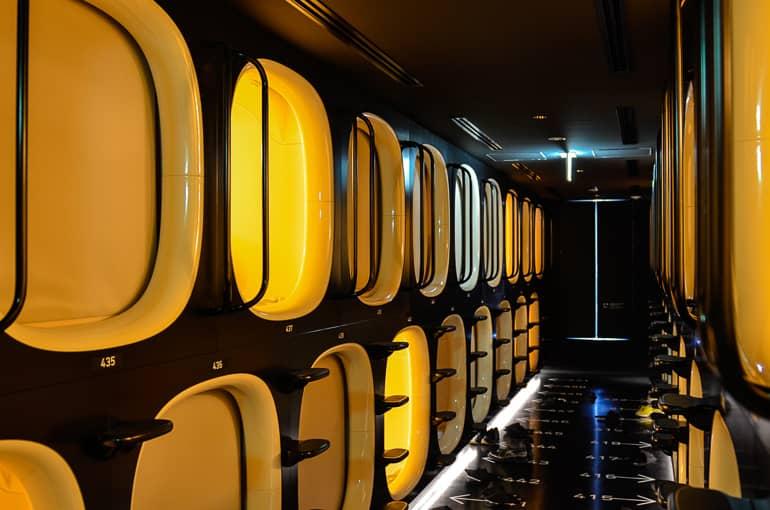 A look inside Tokyo's capsule hotel shows a dark black corridor with many yellow-lit entrances to the sleeping capsules.