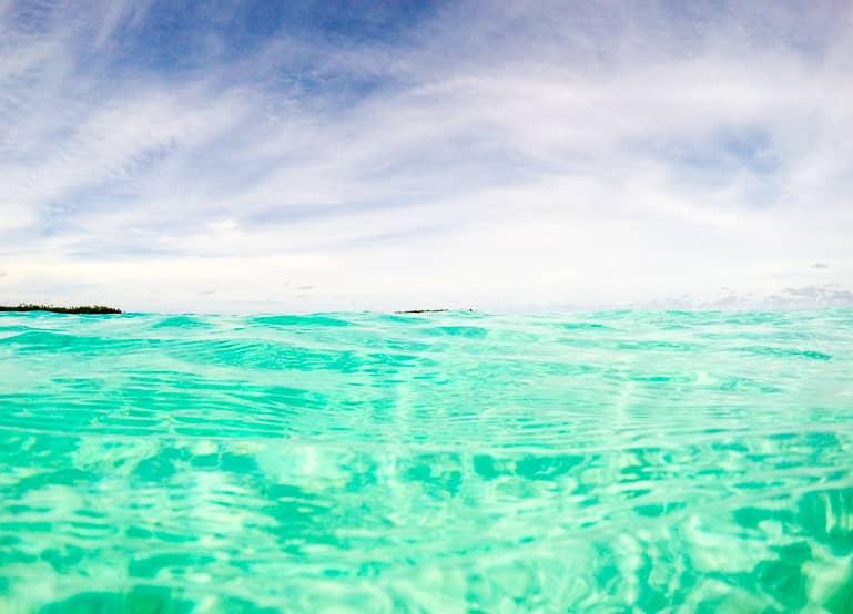 From close up, the green shimmering water of the Cook Island Aitutaki appears crystal clear and invites for snorkeling.