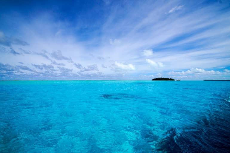 A small island sits in the clear waters of the Cook Islands near Aitutaki, Oceania.
