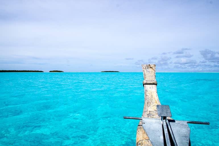 A wooden Vaka sails on the light blue waters of Aitutaki, Cook Islands.